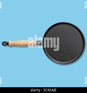 A round, cast iron pan with a wooden handle, ideal for cooking various dishes like pancakes or tortillas. Stock Photo