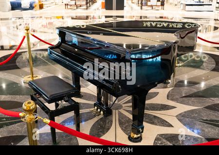 Glossy black grand piano with open lid, displayed in a luxurious public setting with marble floor and red velvet ropes Stock Photo