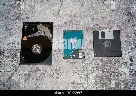 Three data storage devices, a 3.5 inch hard drive, a 2.5 inch hard drive, and a floppy disk arranged in a line on a concrete surface Stock Photo