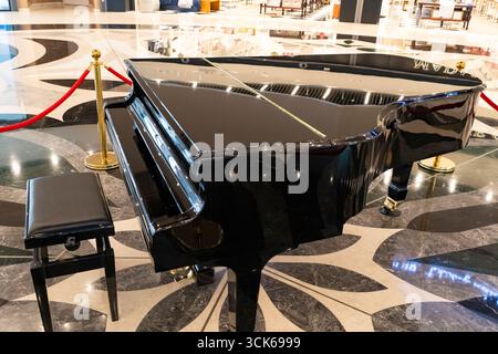 Glossy black grand piano with open lid, displayed in a luxurious public setting with marble floor and red velvet ropes Stock Photo