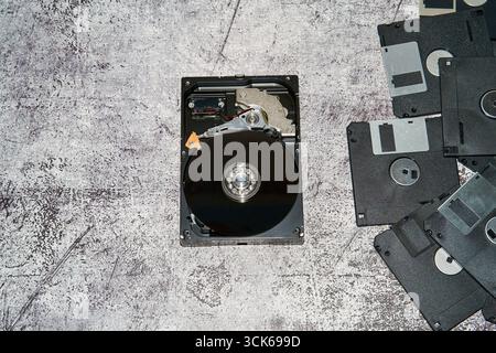 An open 3.5 inch hard disk drive alongside multiple floppy disks on a gray surface. Stock Photo