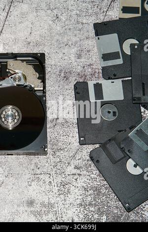 An open 3.5 inch hard drive next to several floppy disks on a grayish surface Stock Photo