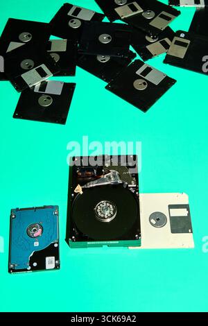 A mix of old floppy disks and hard drives, remnants of different technological ages, stand out against a turquoise backdrop Stock Photo