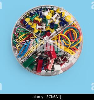 A clear container divided into sections, filled with various office supplies like push pins, paper clips, rubber bands, and binder clips. Stock Photo