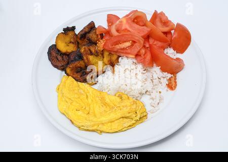 Simple Cuban style food, rice and beans, deep fried banana, tomato salad and an egg omelete Stock Photo