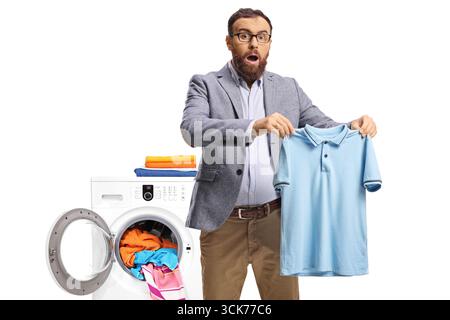 Surprised man holding a small t-shirt in front of a washing machine isolated on white back Stock Photo