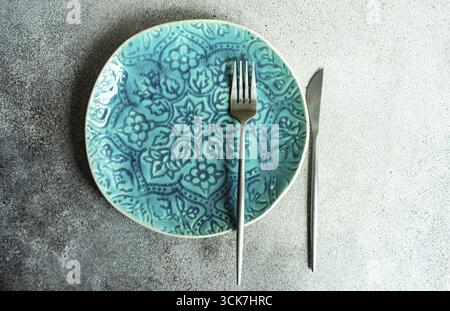Minimalistic place setting with ceramic plate and modern cutlery set on concrete background Stock Photo