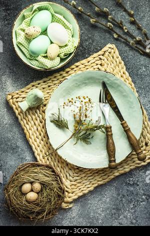 Festive holiday table setting for Easter dinner decorated with colored eggs on stone background with copy space Stock Photo