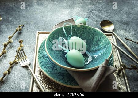 Festive holiday table setting for Easter dinner decorated with colored eggs on stone background with copy space Stock Photo