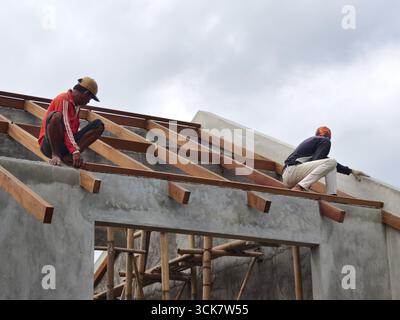 Badung, Bali, Indonesia – September 5, 2025: Construction workers installing wooden roof beams on a building under construction Stock Photo