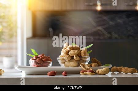 Peeled and unpeeled peanuts in glass bowls on a white plate on a table with a white isolated background. Front view. Stock Photo