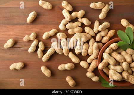 Peanuts with skin in a clay container and on a rustic wooden table. Top view Stock Photo
