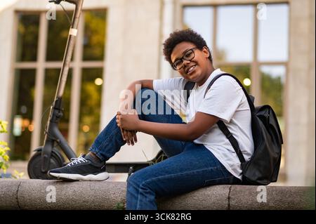 After school. Smiling curly-haired teen with a backpack and in eyeglasses Stock Photo