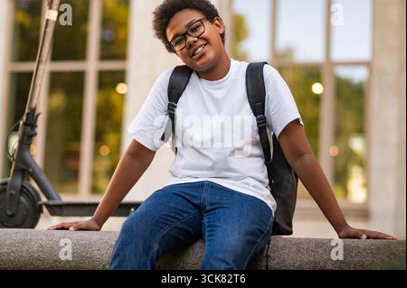 Smiling curly-haired teen with a backpack and in eyeglasses Stock Photo