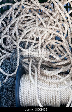 The texture of a spiral white rope wound around a drum and scattered nearby in a pile with chains. Stock Photo