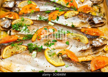 Baked trout fish with slices of lemon, tomatoes, onions, dill and parsley in spices on a tray close-up. Stock Photo