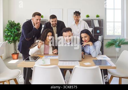 Happy gathering in office, diverse group of colleagues looking intently at laptop screen Stock Photo