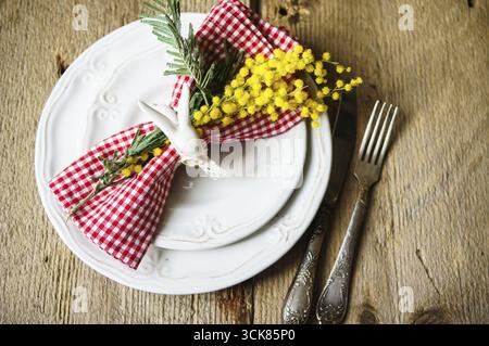 Spring festive dining table setting with yellow mimosa flowers, candles, napkins and vintage cutlery on a wooden board Stock Photo