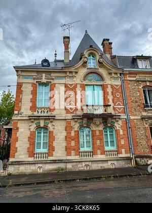 Elegant European historic facade with red brick, light stone, blue shutters, ornate carvings, and steep slate roof with dormer windows Stock Photo