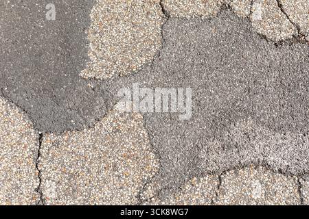 Asphalt pavement with textured aggregate and visible cracks. Abstract pattern formed by cracked and repaired asphalt, showcasing contrasting aggregate Stock Photo