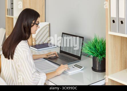 Woman accountant calculating finances, seated at office desk with laptop Stock Photo