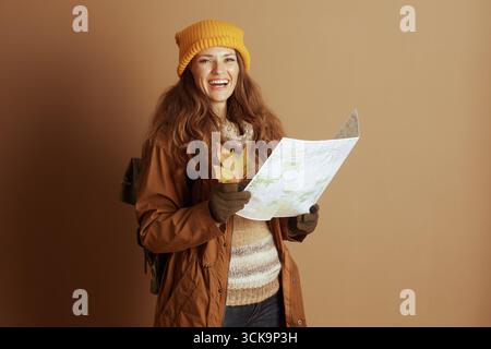 A woman in autumn attire, wearing a yellow beanie and striped sweater, smiles at the camera while holding a map and a fall leaf, embodying seasonal ex Stock Photo
