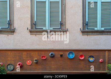 Decorative colorful ceramic plates and bowls arranged on a house wall in Ribeauville, Alsace. Stock Photo