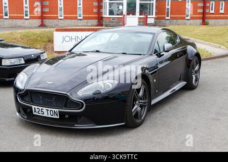 A sleek black sports car Aston Martin Vantage V8 , parked outdoors with modern brick buildings in the background Stock Photo