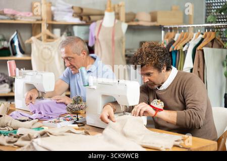 Two tailors sitting in a sewing workshop and working Stock Photo