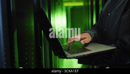 Typing Korean IT tech operating laptop in data center aisle, with server racks, green LED lights Stock Photo