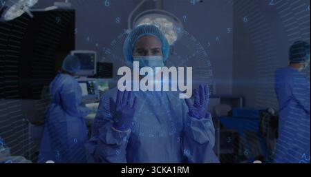 Standing surgeon and assisting team working in operating room, with surgical lights, monitors Stock Photo