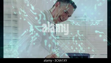 Smiling professional leaning over desk working on laptop in office, with circuit-pattern overlay Stock Photo