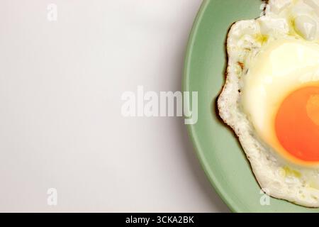A fried egg on a pastel green plate on a pastel purple background. Close-up Stock Photo