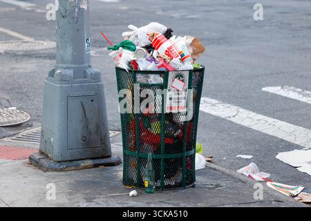 A dirty garbage can filled with litter and trash on a New York City sidewalk. Stock Photo