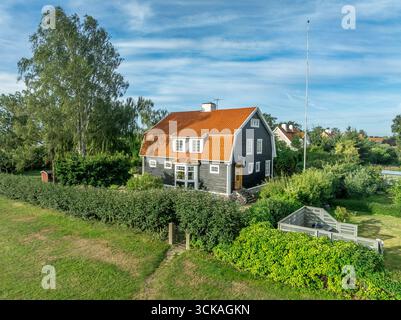 Classic Swedish home in Kalmar with dark grey siding, red dutch gable roof against blue cloudy sky Stock Photo