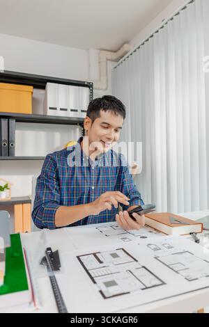 A young architect works on house design plans at his desk, focusing on drawings and scale models. The scene conveys creativity, dedication, and precis Stock Photo