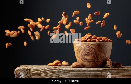 Almond is poured into a wooden bowl. Nuts in motion. Copy space. Stock Photo