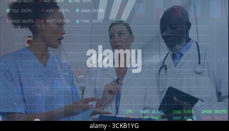 Collaborating medics reviewing digital charts on tablets in hospital corridor with stethoscope, pen Stock Photo