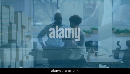Examining tablet two colleagues standing by desk in open-plan office, with storage cabinets Stock Photo