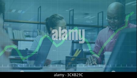 Two coworkers reviewing financial data, working on laptops in office, with documents and coffee cup Stock Photo