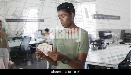 Designer inspecting pink geometric prototype at desk in open plan office, with monitors. Collaboration, innovation, workspace, technology, creativity, Stock Photo