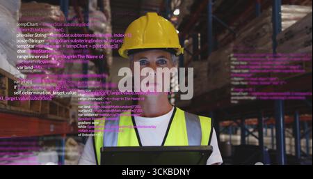 Warehouse manager wearing yellow hard hat, vest scanning tablet in warehouse, with code overlay. Industrial, logistics, organization, digital, efficie Stock Photo