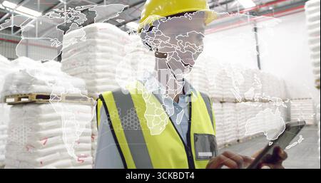Worker wearing safety gear reviewing inventory on tablet in warehouse, with bulk bags, map overlay. Industrial, logistics, inventory, technology, mana Stock Photo