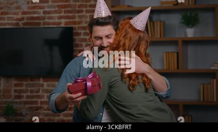 Two Caucasian friends couple at home party birthday congratulation woman congratulate man giving present box festive gift surprise excited male Stock Photo