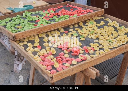 Handmade orecchiette pasta in vibrant colors drying on rustic wooden trays, typical Italian culinary tradition. Stock Photo