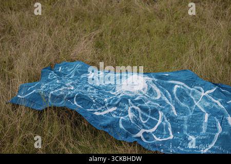 A blue fabric laid on grass, featuring white abstract patterns and text, evoking a sense of nature and art Stock Photo