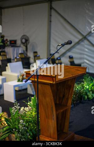 A wooden podium with a microphone set up for a speech, surrounded by plants and chairs in a tented venue Stock Photo