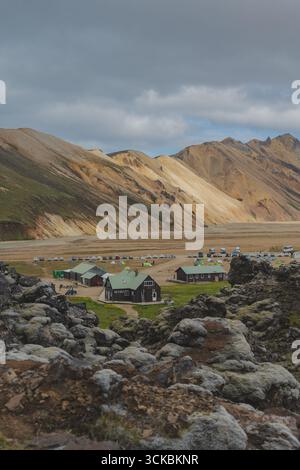 A small settlement with green roofed buildings and parked vehicles in Landmannalaugar, Iceland, framed by moss covered lava rocks and colorful mountai Stock Photo