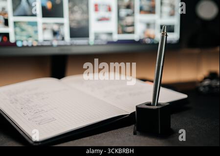 Metal pen in holder on desk with open notebook and blurred computer screen in background. Minimal modern workspace concept. Stock Photo