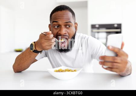 Man Enjoying Breakfast While Using Smartphone in Modern Kitchen Stock Photo